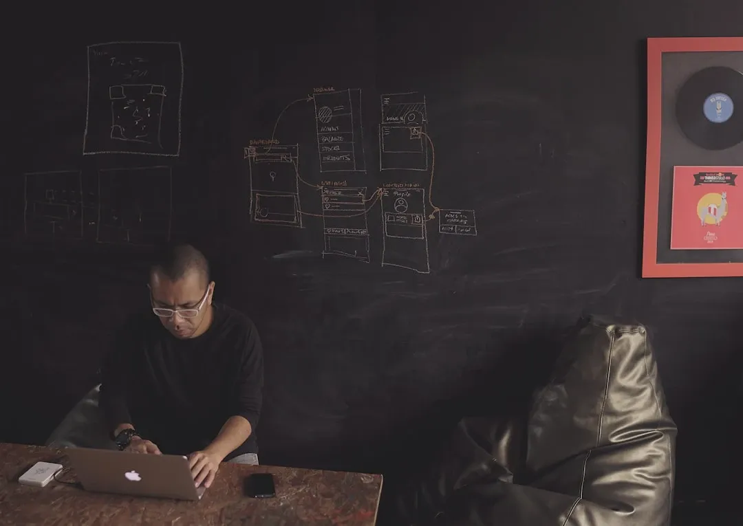 man sitting near table facing gray MacBook